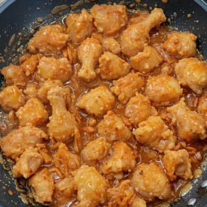 Crispy chicken coated in a glossy sweet chili glaze, served with lime wedges and fresh herbs.